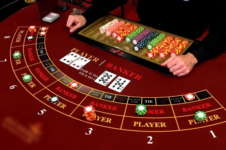빨간색 바탕의 로즈카지노 바카라 게임 테이블.7가지 색의 칩과 플레이어,뱅커 카드가 오픈되어 있는 바카라 이용 룰에 대한 이미지.